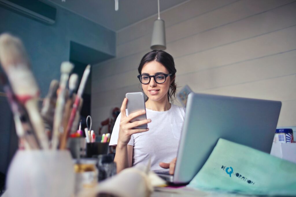 Kein Digital Detox: Frau sitzt mit Smartphone vorm Laptop