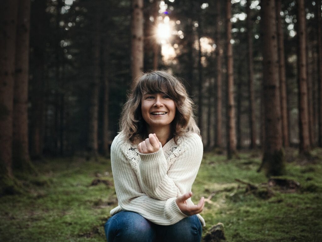 Hannah Assil sitzt auf dem Boden im Wald und lacht.