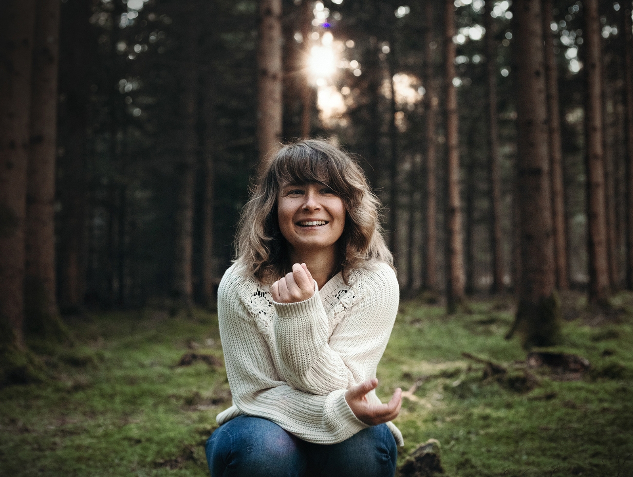 Hannah Assil sitzt auf dem Boden im Wald und lacht.