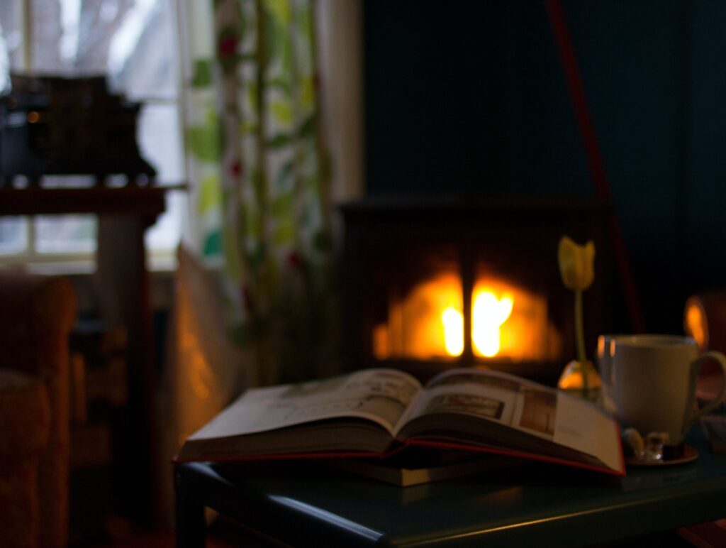 Ein Buch liegt aufgeschlagen vor einem Kamin. Daneben steht eine Teetasse.